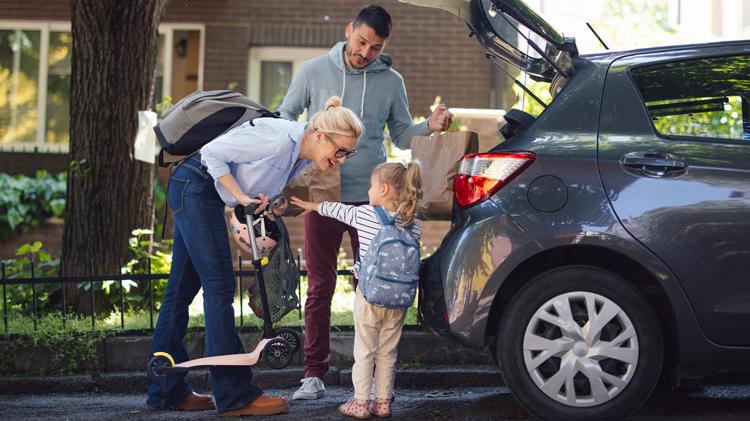 A family of three unpacks groceries from the back of their SUV.