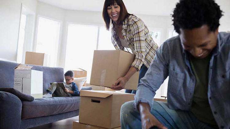 A couple unpack while their son reads on the couch.