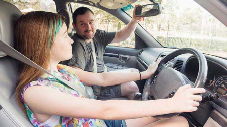 Dad adjusts the rearview mirror for his daughter instructing her on the proper angles.